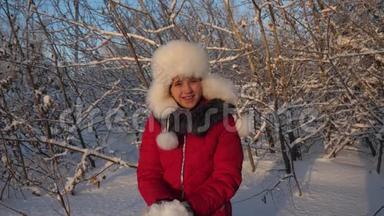 美丽的少女在冬季公园玩耍。 幸福的女孩在森林日落时用手举起雪。 白雪皑皑